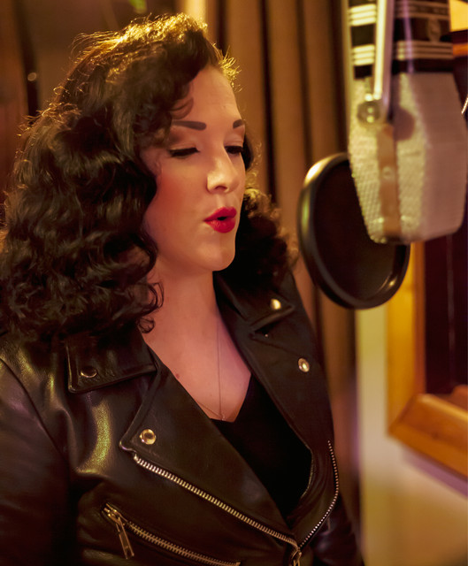 Kelsey Rae Copeland in a black leather jacket singing into a vintage ribbon microphone